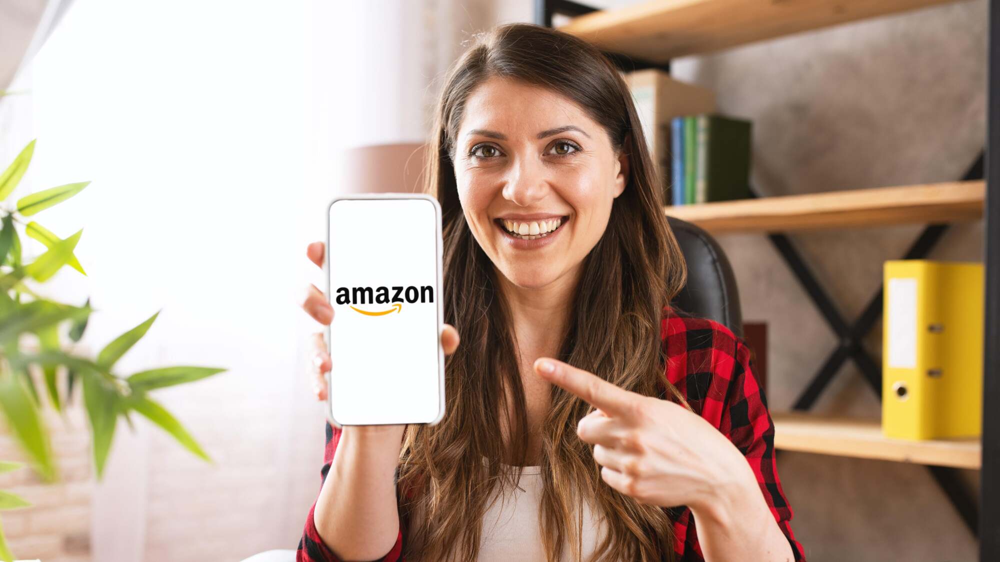 A woman with vacant eyes pointing to an Amazon logo on her smartphone's screen and smiling a hollow smile