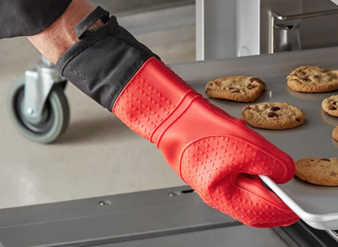 A red oven mitt clad hand holding a sheet of cookies.