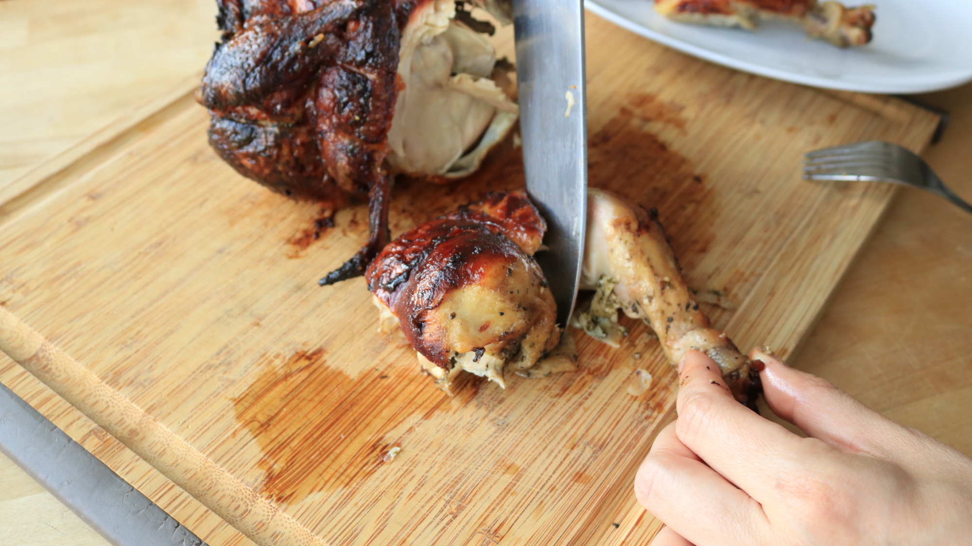 A knife cutting a chicken thigh.