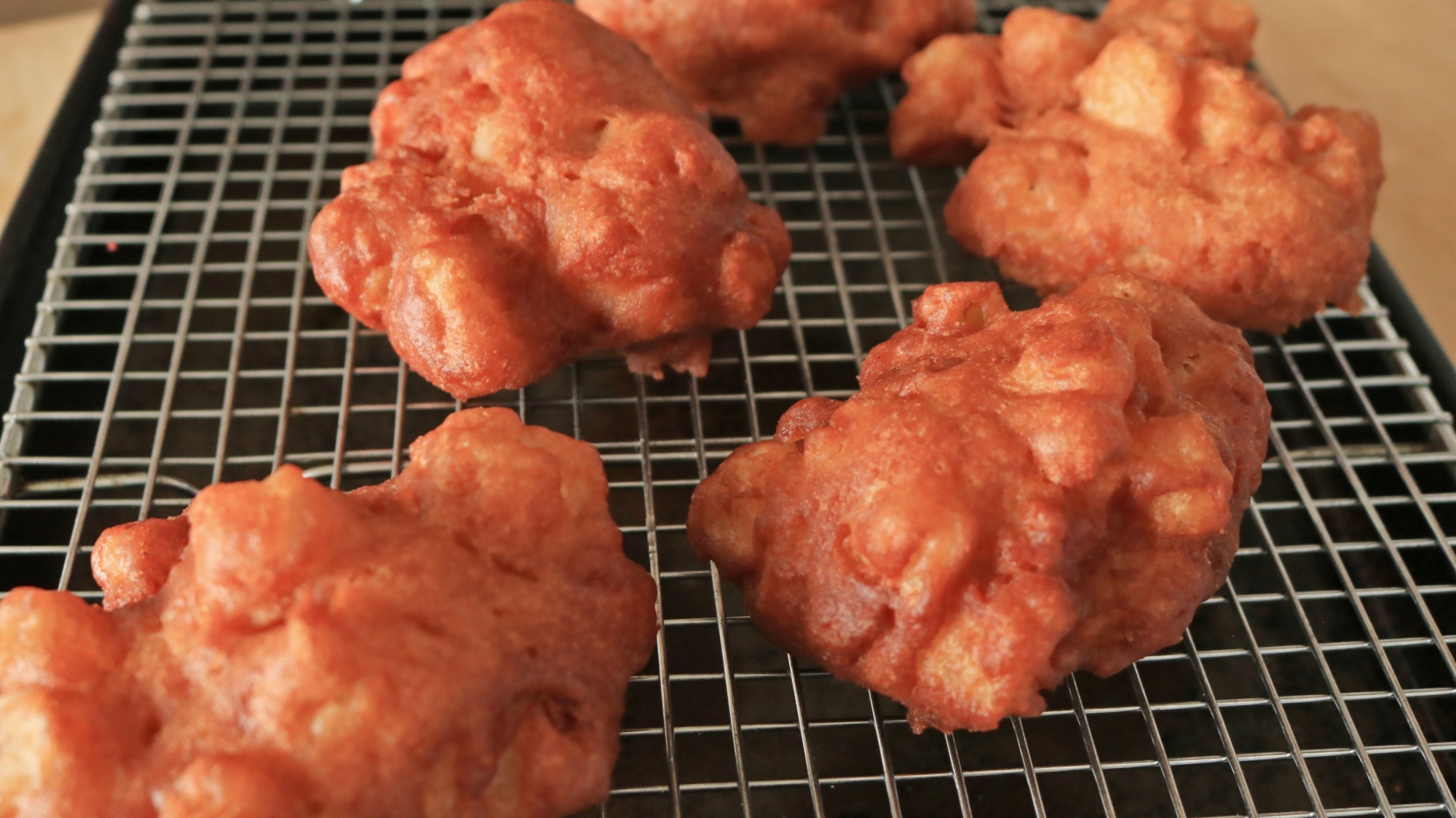 Freshly fried apple fritters on a wire rack cooling.