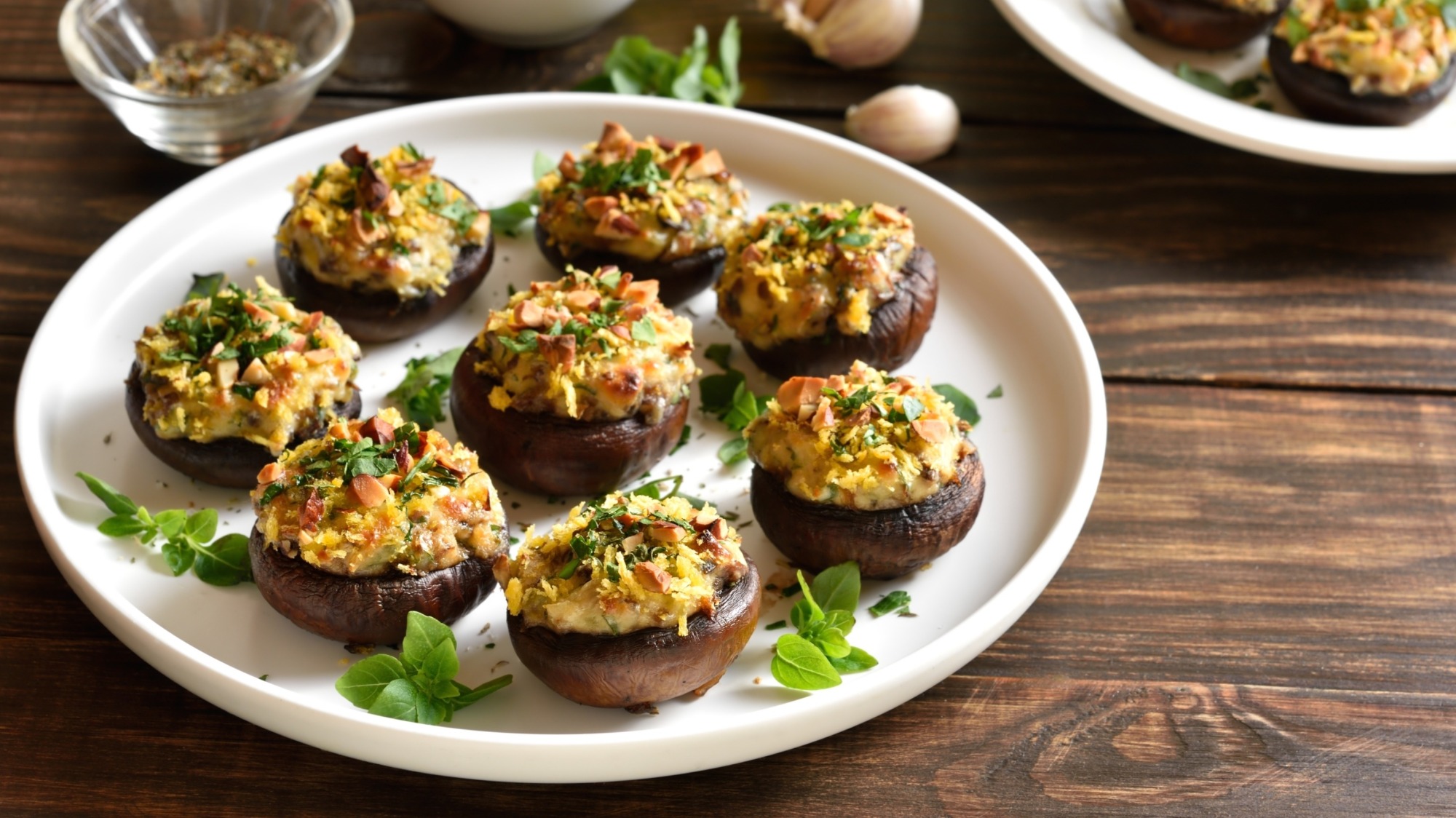 A white plate full of stuffed mushrooms on a wood table.