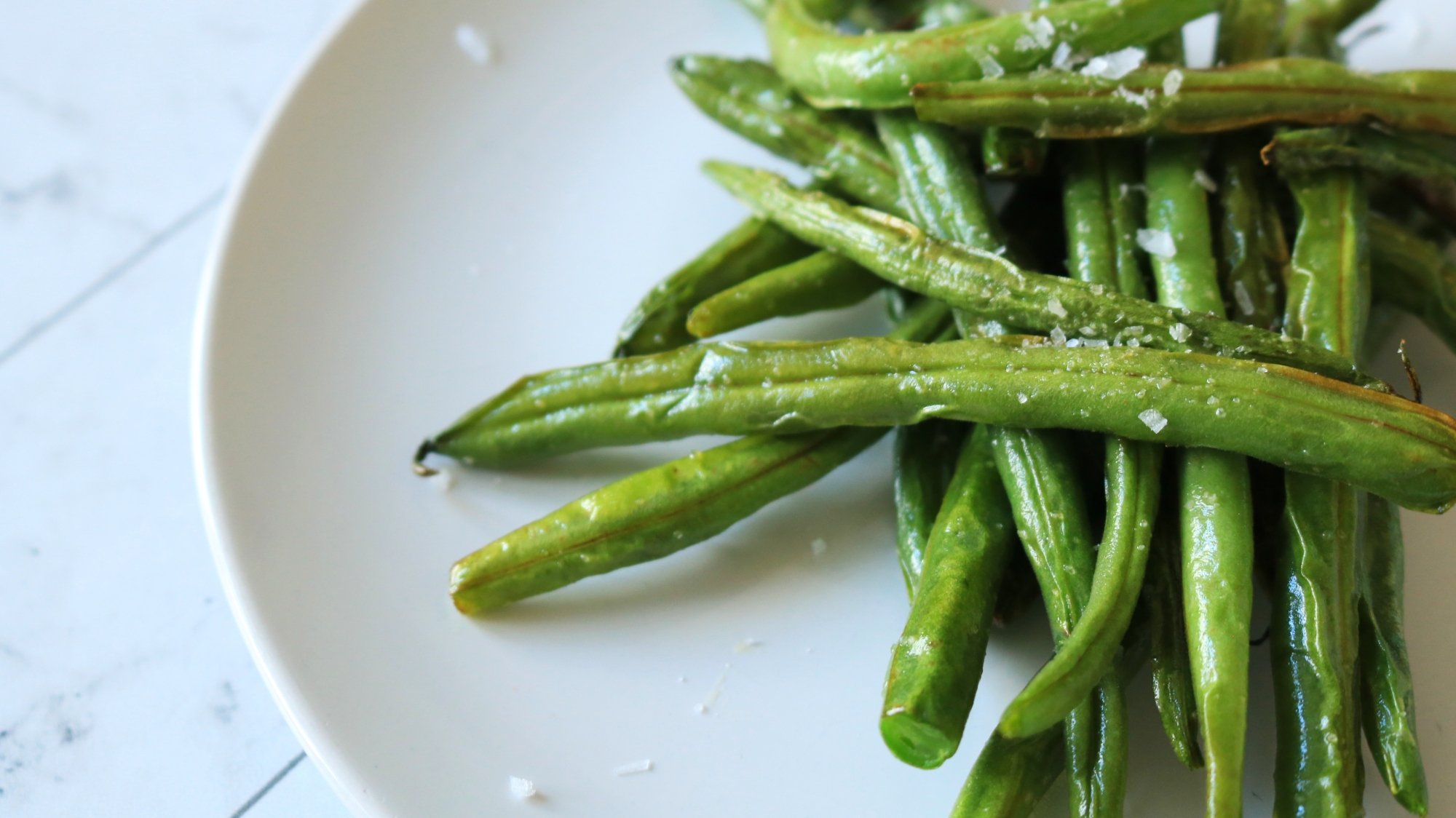 Roasted green beans sprinkled with salt on a plate.