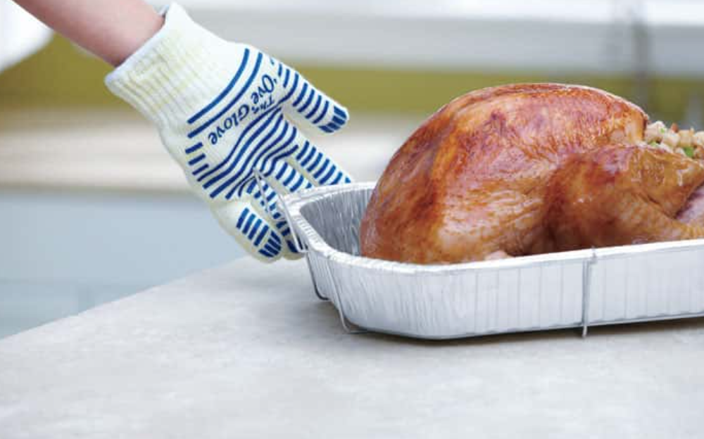 An oven mitt covered hand reaching for a roasted turkey in a tray.