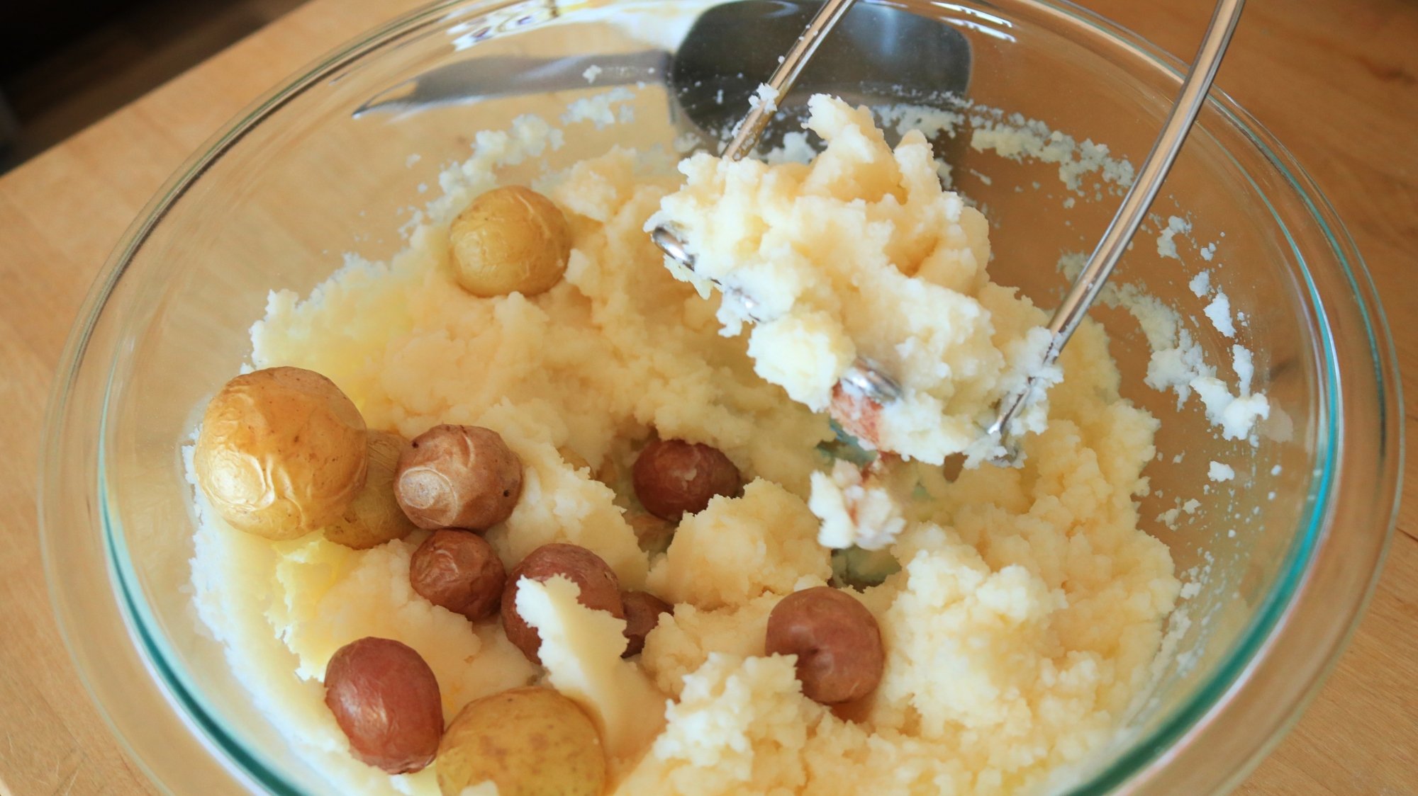 A potato masher in a bowl of instant mashed potatoes and air fried baby potatoes.